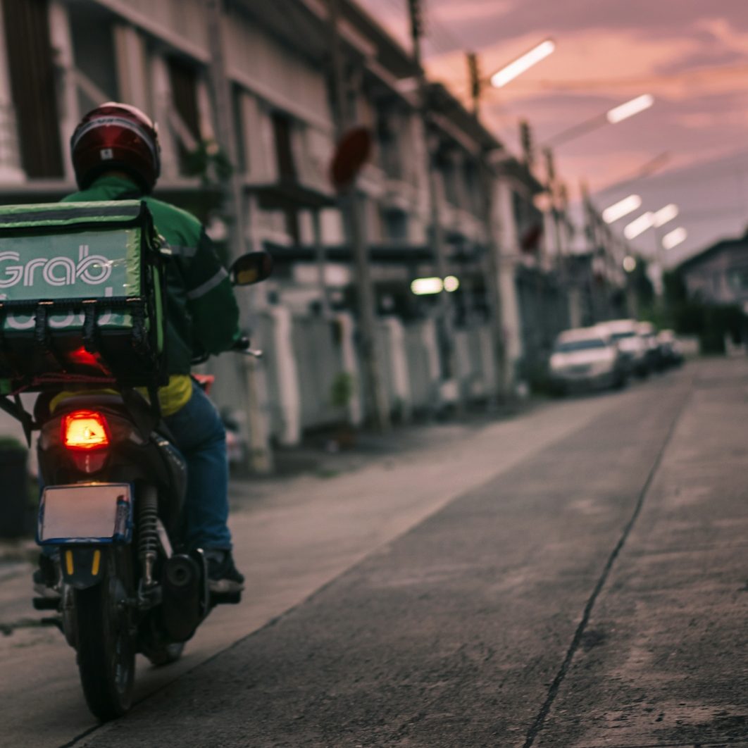 A pot delivery rider on a motorcycle in a street during sunset with city lights.